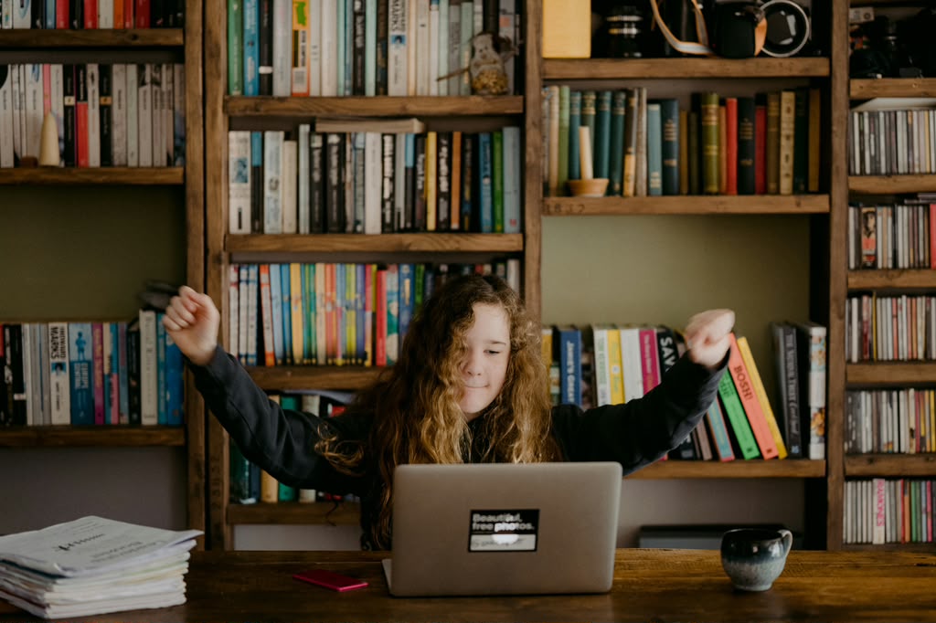 Student celebrating with arms raised at her laptop
